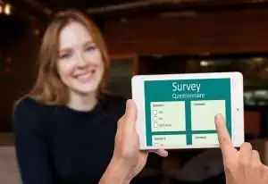 Person smiling while holding a tablet displaying a survey questionnaire, emphasizing data collection in business contexts related to data protection and compliance.