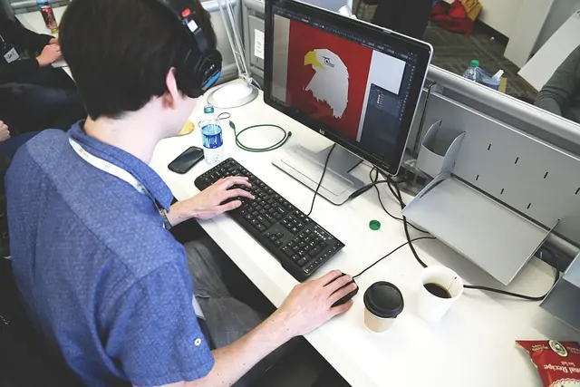 Person working on a computer with graphic design software, creating an illustration of an eagle, in a modern office setting, emphasizing digital creativity and design skills.