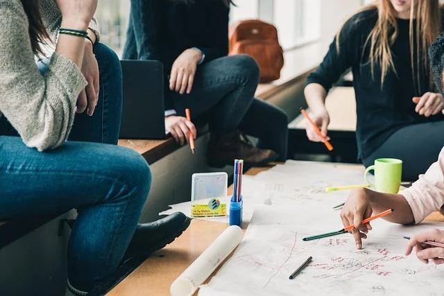 Group of people collaborating on a project, using pens and markers on large paper sheets, with a focus on teamwork and brainstorming for ISMS implementation.