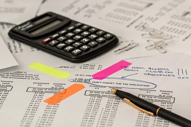 Calculator on financial documents with highlighted notes and a pen, emphasizing investment analysis and tax implications related to ISO certification processes.