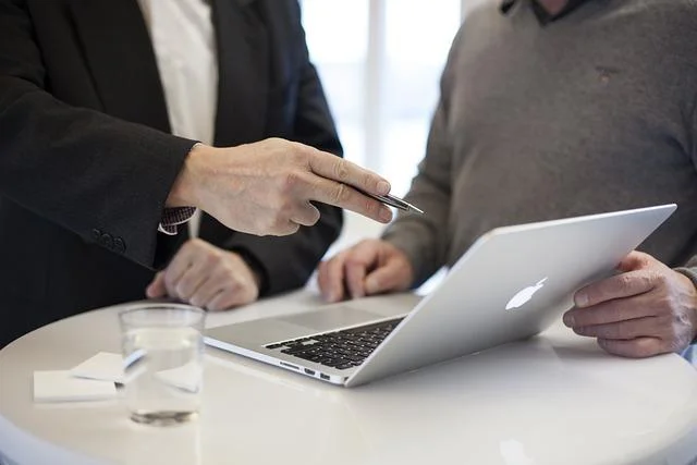 Business professionals discussing ISO 42001 certification process over a laptop, with a focus on consultation and documentation.