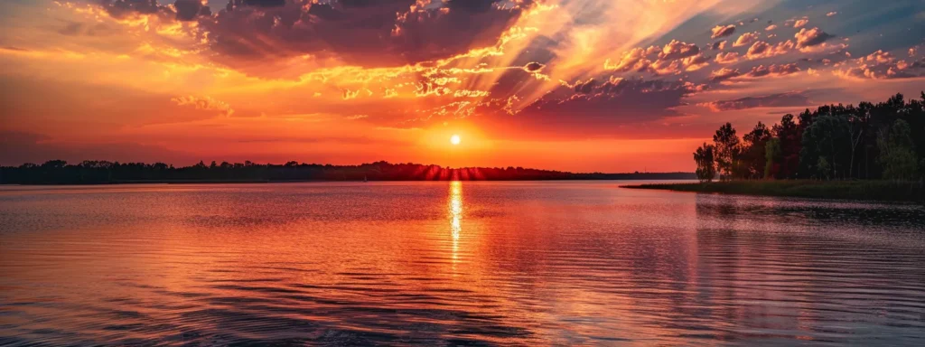 ein majestätischer sonnenuntergang über einem ruhigen see, wo das orange und rote licht sanft auf der glitzernden wasseroberfläche reflektiert und eine friedliche atmosphäre schafft.