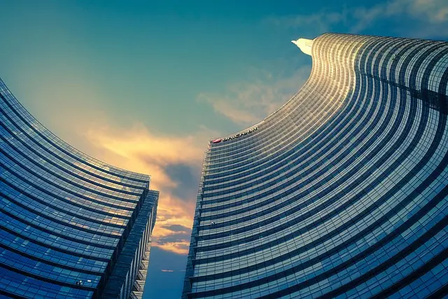 Moderne Bürogebäude mit geschwungener Architektur und reflektierenden Fenstern unter einem blauen Himmel mit Wolken, symbolisierend die Anforderungen an IT-Infrastruktur und Compliance in der Unternehmenswelt.
